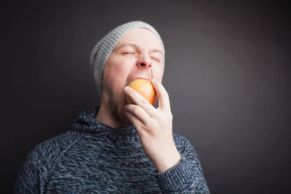 El tipo del sombrero se come una manzana roja sobre un fondo negro en el estudio — Foto de Stock