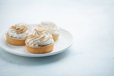 Beyaz vintage tabakta beze ile lezzetli limon tartlets. Tatlı ışık mavi bir arka plan üzerinde tedavi. kopya alanı