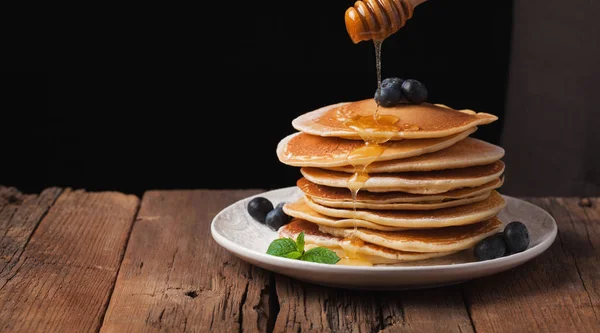 The chef pours honey pancake stack with blueberries and mint on black background. Copy space for your text — Stock Photo, Image