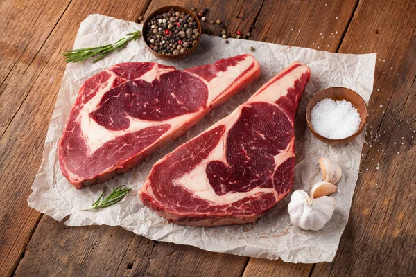 Dvě čerstvé syrové mramorové maso, black Angus ribeye steak s kořením na staré rustikální stůl. Syrové hovězí maso na dřevěné pozadí — Stock fotografie