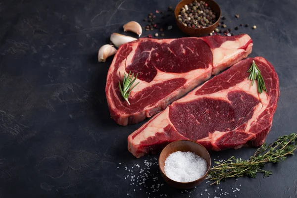 Rauw vers Gemarmerde vlees Steak Ribeye Black Angus op zwart marmeren achtergrond. Rundvlees met kruiden op een donkere stenen tafel. Bovenaanzicht met kopie ruimte — Stockfoto