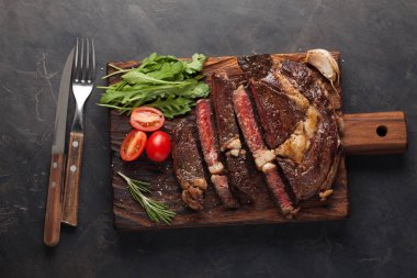 Izgara antrikot biftek biftek, otlar ve baharatlar karanlık bir taş zemin üzerine. Üstten Görünüm