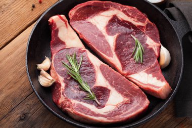 İki taze çiğ mermer et, kara Angus eti biftek demir içinde baharatlar ile eski bir rustik masaya pan. Ahşap arka plan üzerinde ham sığır eti. Üstten Görünüm