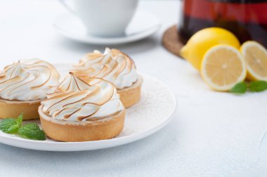 Limon beze vintage beyaz tabak ve bardak çay taş masanın üzerine ile tartlets. Açık mavi arka planı üzerinde lezzetli tedavi