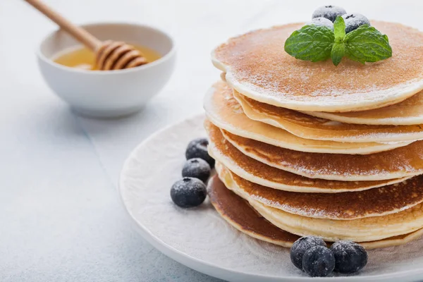 A stack of delicious pancakes with honey and blueberries on a light blue background — Stock Photo, Image