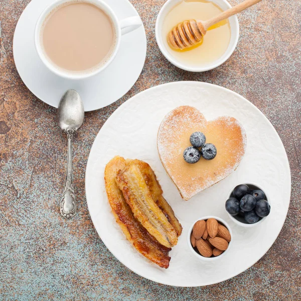 一堆美味的煎饼与蜂蜜, 咖啡和蓝莓在一个生锈的红色背景上。情人节的早餐很丰盛。顶部视图 — 图库照片