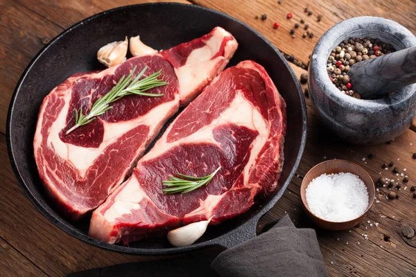 Dvě čerstvé syrové mramorové maso, black Angus ribeye steak s kořením v železnou pánev na staré rustikální stůl. Syrové hovězí maso na dřevěné pozadí. Pohled shora — Stock fotografie