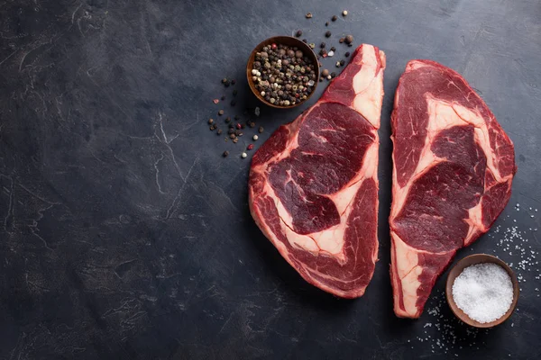Čerstvé syrové mramorované maso Steak Ribeye Black Angus na černém mramorovém pozadí. Hovězí maso s kořením na temný kamenný stůl. Pohled shora s kopií prostor — Stock fotografie