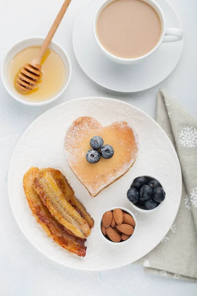 Egy halom finom palacsintát, méz, a kávé és a fekete áfonya, a világos kék háttér. Reggeli a Valentin-nap. Szemközti nézet — Stock Fotó