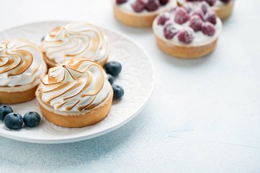Ahududu ve lezzetli limon beze beyaz vintage tabakta ile tartlets. Tatlı ışık mavi bir arka plan üzerinde tedavi