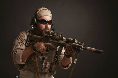 Acımasız adam askeri çöl üniforma ve vücut zırh mücadele bir rafa anlamına gelir ve bir siyah arka plan üzerine tüfeğini tutar. Amaçlayan bir tüfek airsoft koruyucu gözlük sakallı Player'da