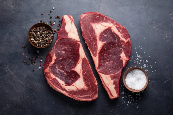 Raw fresh marbled meat Steak Ribeye Black Angus on black marble background. Beef with spices on a dark stone table. Top view