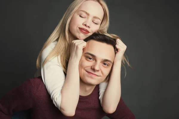 Portrait d'un beau jeune couple amoureux posant en studio sur fond sombre. Fille assise sur les épaules d'un jeune homme et le tient par les cheveux — Photo