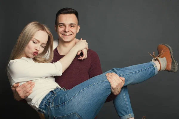 Portrait d'un beau jeune couple amoureux posant en studio sur fond sombre. Le mec tient sa bien-aimée dans ses bras et sourit — Photo