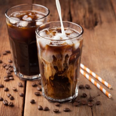 Krem üzerine dökülür ve bir eski rustik ahşap masa üzerinde kahve çekirdekleri ile uzun bir bardak buzlu kahve. Koyu ahşap arka plan üzerinde soğuk yaz içeceği