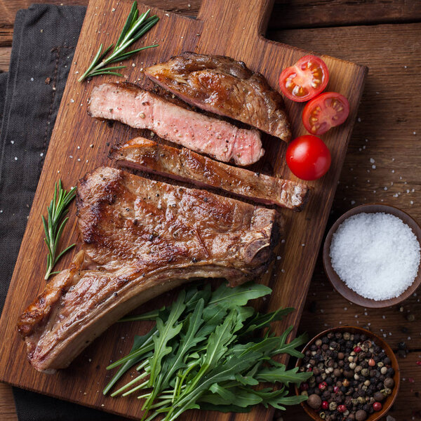 Grilled cowboy beef steak, herbs and spices on a rustic wooden background. Top view.