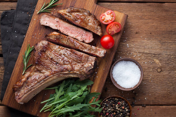 Grilled cowboy beef steak, herbs and spices on a rustic wooden background. Top view with copy space for your text.