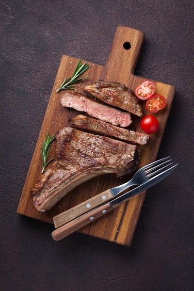 Bife grelhado de vaca cowboy, ervas e especiarias em um fundo de pedra escura. Vista superior — Fotografia de Stock