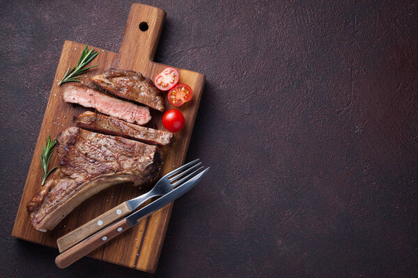 Grilled cowboy beef steak, herbs and spices on a dark stone background. Top view with copy space for your text.