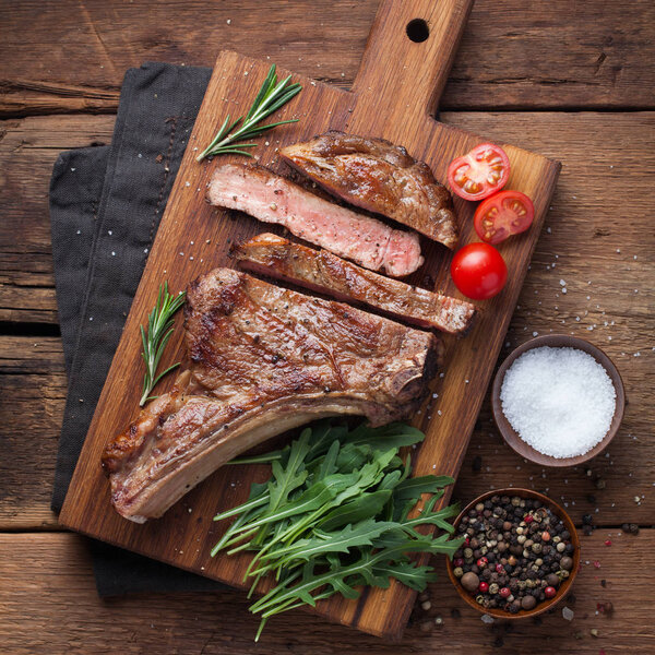 Grilled cowboy beef steak, herbs and spices on a rustic wooden background. Top view.