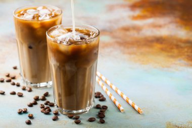 Büyük bardakta buzlu kahve, üstüne krema dökülmüş ve kahve çekirdekleri. Mavi paslı arka planda fotokopi alanı olan soğuk yaz içeceği