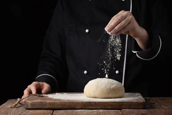 Chef manos verter harina en polvo sobre la masa cruda utilizando tamiz sobre un fondo negro, proceso de cocción — Foto de Stock