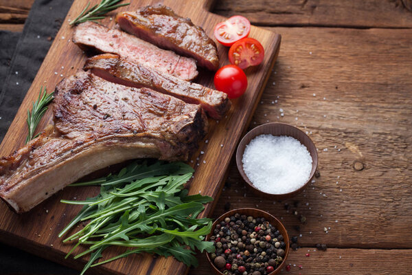 Grilled cowboy beef steak, herbs and spices on a rustic wooden background. Top view with copy space for your text.