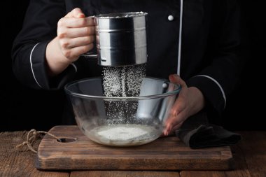 Şef dökme un tozu elek üzerinde siyah bir arka plan kullanarak, işlem yemek çiğ hamur üzerinde eller