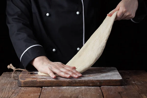 Chef amasando masa, haciendo masa por manos femeninas en la panadería sobre un fondo negro — Foto de Stock