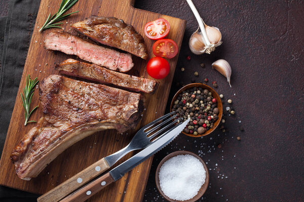 Grilled cowboy beef steak, herbs and spices on a dark stone background. Top view with copy space for your text.