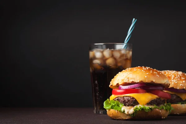Nahaufnahme von köstlichen frischen hausgemachten Burgern mit Salat, Käse, Zwiebeln, Tomaten und Cola mit Eis auf dunklem Hintergrund mit Kopierraum — Stockfoto
