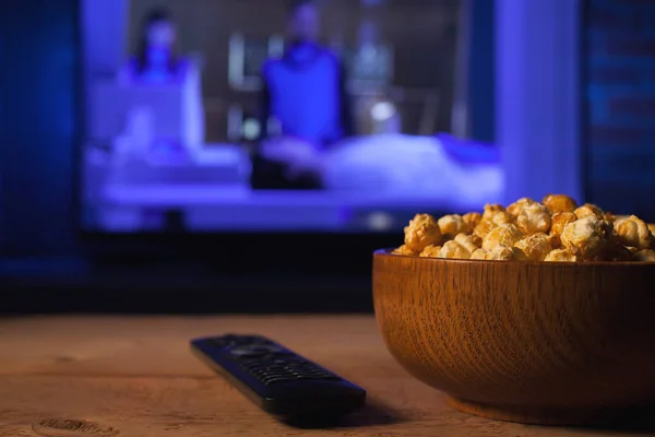Arkaplanda bir kase patlamış mısır ve uzaktan kumanda var. Televizyon çalışıyor. Akşam sıcacık, evde film ya da TV dizisi seyrediyor.