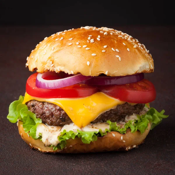 Közeli kép a finom friss házi készítésű burger saláta, sajt, hagyma és a paradicsom, a sötét háttér előtt. Fast food és szemét élelmiszer koncepció — Stock Fotó