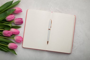 Boş Not Defteri ile hafif taş zemin üzerine kalem ve pembe laleler