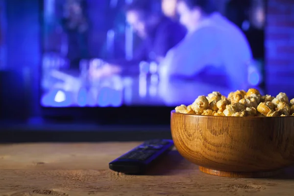 Eine hölzerne Schüssel Popcorn und Fernbedienung im Hintergrund funktioniert der Fernseher. Abends gemütlich einen Film oder eine Fernsehserie zu Hause anschauen — Stockfoto