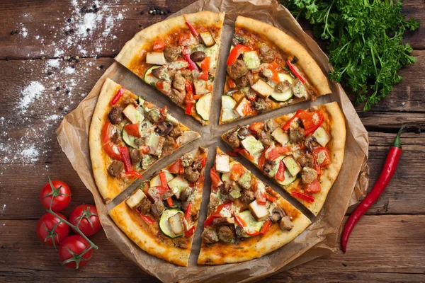 Homemade vegan pizza with tomatoes, zucchini, bell peppers, mushrooms and soy meat on an old wooden table. Top view