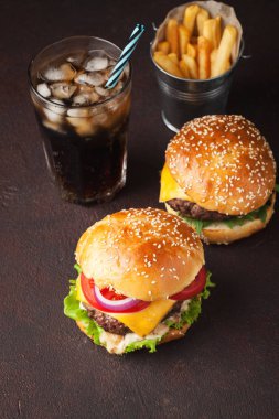 Marul, peynir, soğan, domates ve karanlık bir arka plan üzerinde buzlu cola ile lezzetli taze ev yapımı hamburger Close-Up