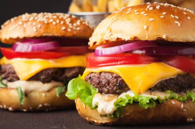Marul, peynir, soğan ve domates karanlık bir arka plan üzerinde lezzetli taze ev yapımı hamburger close-up. Fast food ve abur cubur kavramı