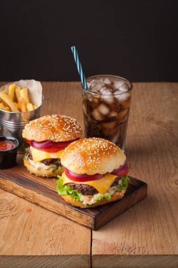 Marul, peynir, soğan ve domates bir rustik ahşap tahta üzerinde lezzetli taze ev yapımı hamburger close-up. Ayrıca patates ve ahşap bir masa üzerinde buzlu Cola