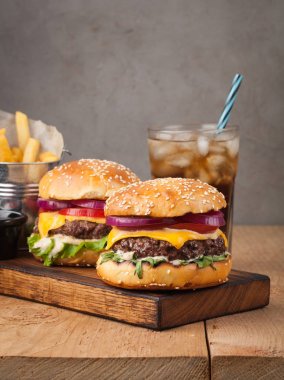 Marul, peynir, soğan ve domates bir rustik ahşap tahta üzerinde lezzetli taze ev yapımı hamburger close-up. Ayrıca patates ve ahşap bir masa üzerinde buzlu Cola