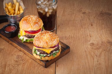 Marul, peynir, soğan ve domates bir rustik ahşap tahta üzerinde lezzetli taze ev yapımı hamburger close-up. Ayrıca patates ve kopya alanı ile ahşap bir tabloda buzlu Cola