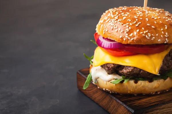 Вкусный домашний гамбургер на гриле с говядиной, помидорами, сыром, огурцом и салатом на темном каменном фоне с копировальным пространством — стоковое фото