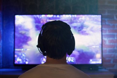 Oyun veya kulaklık mikrofon ile flama karanlık odada evde oturuyor ve video oyunları ağlarda arkadaşlarınızla çalış. Monitör veya Tv önünde genç bir adam oturuyor