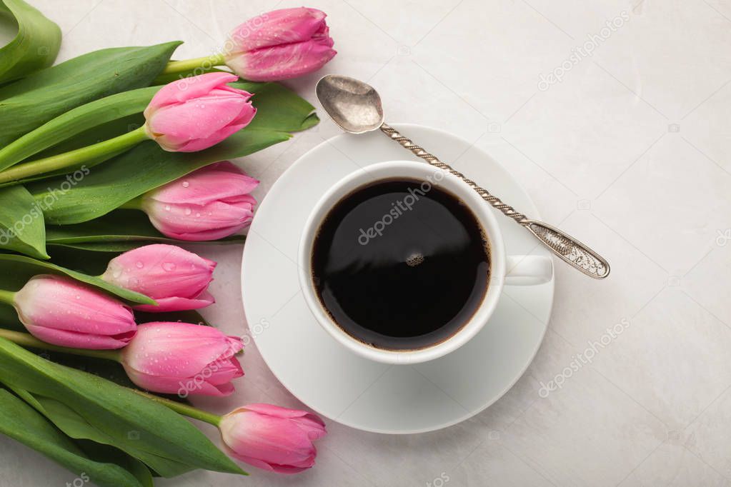 Black coffee in white Cup with pink tulips on light stone background. Top view