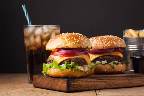 Primer plano de deliciosa hamburguesa casera fresca con lechuga, queso, cebolla y tomate en una mesa de madera rústica. También patatas fritas y Cola con hielo en una mesa de madera — Foto de Stock