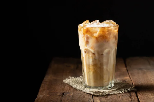 Café helado en un vaso alto con crema vertido y granos de café sobre una vieja mesa rústica de madera. Bebida fría de verano sobre un fondo de madera oscura con espacio para copiar —  Fotos de Stock