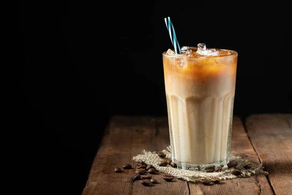 Es kopi dalam gelas tinggi dengan krim dituangkan di atas dan biji kopi di atas meja kayu pedesaan tua. Minuman musim panas yang dingin di latar belakang kayu gelap dengan ruang fotokopi — Stok Foto