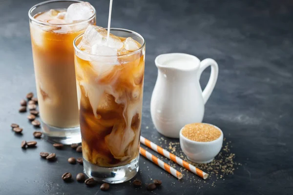 Es kopi dalam gelas tinggi dengan krim dituangkan di atas, gula coklat dan biji kopi. Minuman musim panas yang dingin dengan latar belakang yang gelap. Dengan ruang fotokopi — Stok Foto
