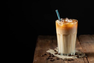 Krem üzerine dökülür ve bir eski rustik ahşap masa üzerinde kahve çekirdekleri ile uzun bir bardak buzlu kahve. Koyu ahşap arka plan kopya alanı ile soğuk yaz içki