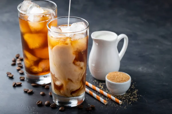 Es kopi dalam gelas tinggi dengan krim dituangkan di atas, gula coklat dan biji kopi. Minuman musim panas yang dingin dengan latar belakang yang gelap. Dengan ruang fotokopi — Stok Foto